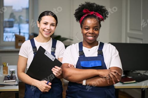 Preview: Young Adult Caucasian Woman and Young Adult Black Woman Smiling in Office Cleaning Uniforms