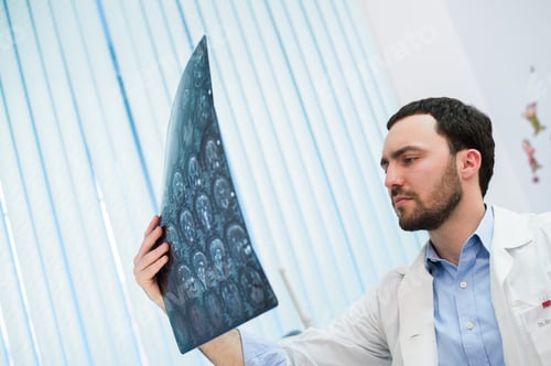 Preview: Closeup portrait of intellectual man healthcare personnel with white labcoat, looking at brain x-ray