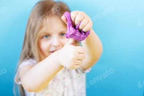 Preview: Blonde girl hold purple slime isolated on a blue background. child playing with a slime toy.