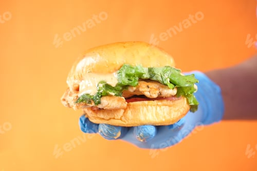 Preview: hand in latex gloves holding beef burger close up