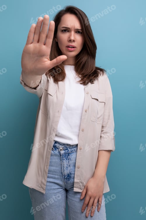 Preview: suspicious caucasian young brunette woman in a shirt and jeans asks to stop on a blue background