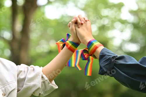 Preview: Cropped shot of homosexual couple wearing rainbow awareness wristbands holding hands.