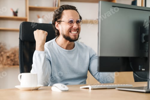 Preview: Image of programmer man making winner gesture working with computer