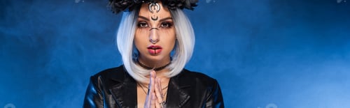 Preview: young woman in witch halloween makeup with praying hands on blue foggy background, banner