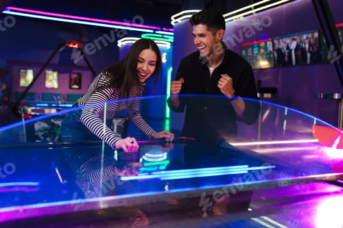 Preview: White young friends laughing while playing air hockey