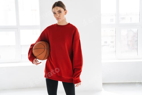 Preview: Athletic young sportswoman working out with basketball indoors