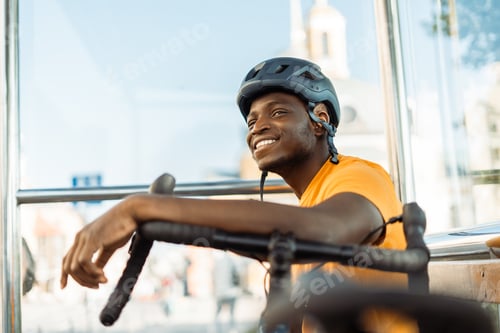 Preview: Smiling african american man looking away while relaxing with bicycle at the bus station