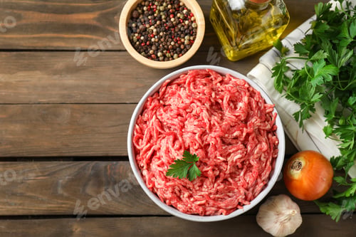 Preview: Raw ground meat in bowl, spices, oil and parsley on wooden table, flat lay. Space for text