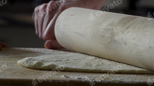 Preview: Man rolling out dough on kitchen table, close up. Scene. The cook rolls a piece of dough on the