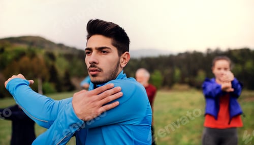 Preview: A portrait of young man with large group of people doing exercise in nature
