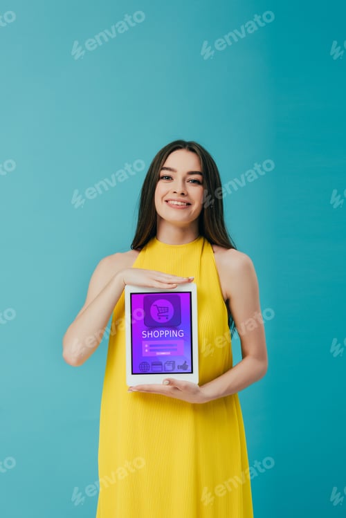 Preview: beautiful brunette girl in yellow dress showing digital tablet with shopping app isolated on