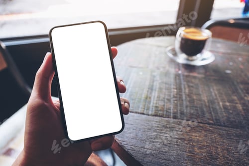 Preview: Mockup image of a hand holding and showing black mobile phone with blank white screen in cafe