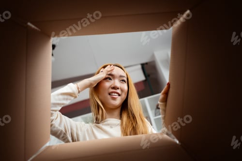Preview: Young Woman Peeking Inside Cardboard Box With Curiosity