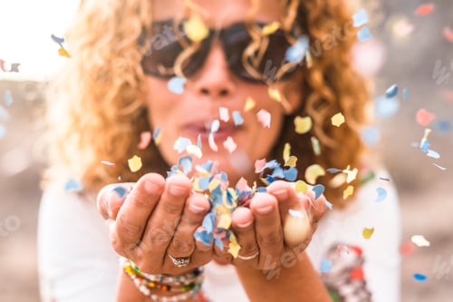 Preview: Close up of woman's habd and beautiful lady blowing out coloured carnival party confetti