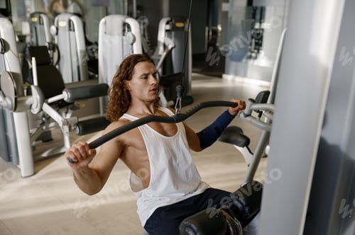 Preview: Motivated young athletic man having workout on gym exercising machine
