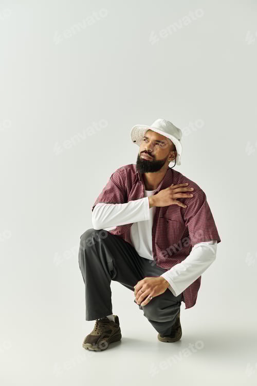Preview: Man in Hat Crouches in Casual Attire