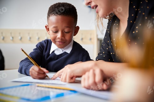 Preview: Female primary school teacher helping a young school boy sitting at table in a classroom