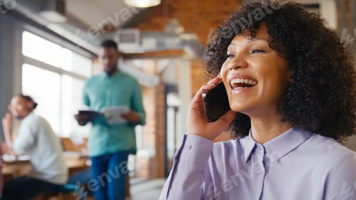 Preview: Businesswoman Talking On Mobile Phone In Busy Open Plan Office With Colleagues In Background