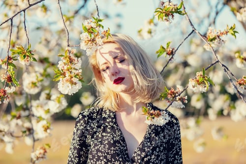 Preview: Blonde girl near blooming tree at countryside in sunset