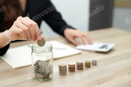 Preview: A close-up picture of a business woman putting a coin in a glass jar To save money and plan for it a
