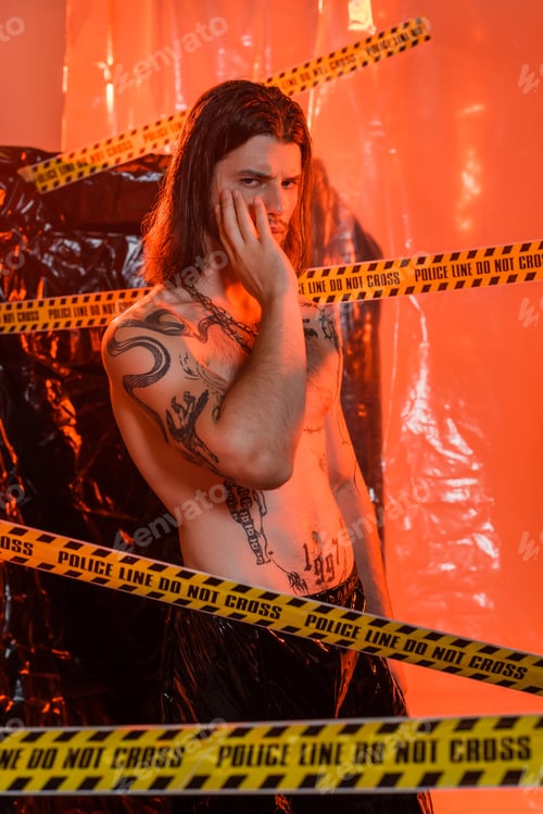 Preview: Shirtless tattooed model touching face near police line and polyethylene at background
