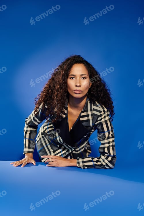 Preview: Dynamic pose of a beautiful woman exuding confidence against a striking blue backdrop