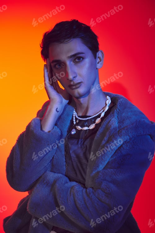 Preview: elegant androgynous man in purple faux fur posing on vibrant backdrop and looking at camera