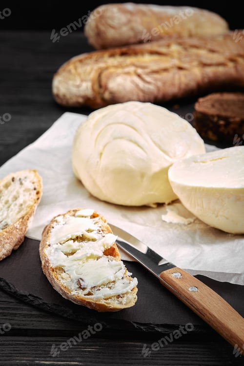 Preview: Loaf of bread with butter and knife. Dark background, side view
