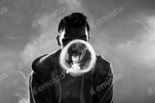 Preview: Black and white photo of young bearded man vaping and making circle from smoke