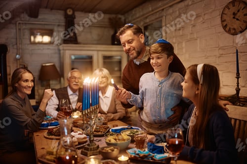 Preview: Happy father and son lighting candles in menorah during family dinner on Hanukkah.
