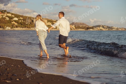 Preview: Back photo of happy couple running along the seashore at sunset