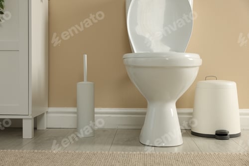 Preview: Toilet bowl, brush and trash bin near beige wall in restroom
