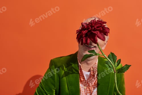 Preview: optimistic and trendy senior male model in green velour blazer hiding behind red peony