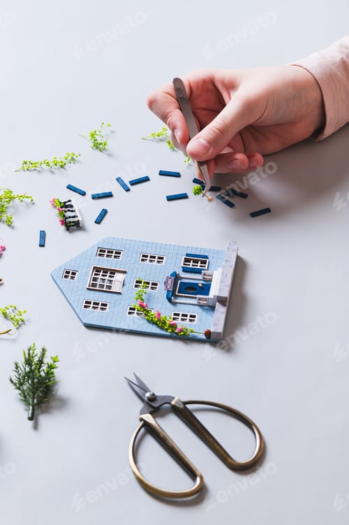 Preview: A child's hand decorates a house figurine with a plant vertical view