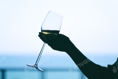 Preview: Silhouette image of a woman's hand holding a wine glass with blurred sea background