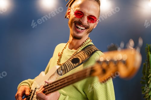 Preview: Young fashionable man in pink sunglasses playing guitar with joy