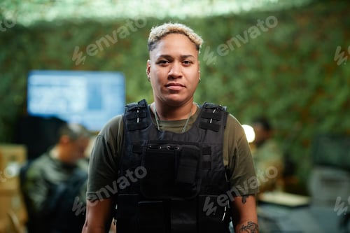 Preview: Young multiethnic female officer in black bulletproof vest looking at camera