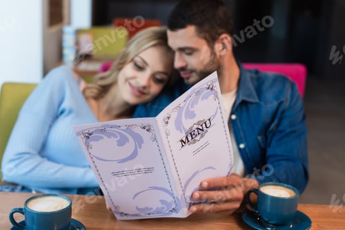 Preview: blurred couple holding menu near cups of coffee in restaurant