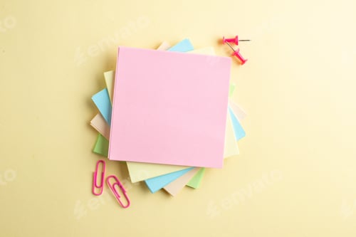 Preview: Overhead view of stacked sticky note cubes and paper clips drawing pins on shaded yellow background