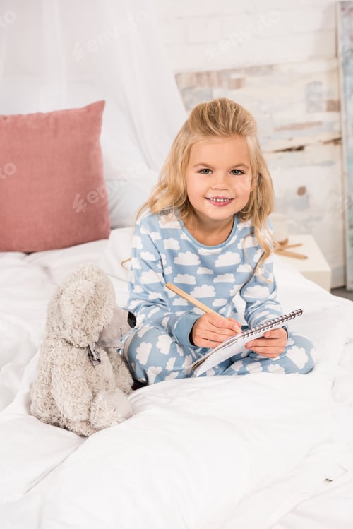 Preview: adorable child sitting in bed and writing in notebook
