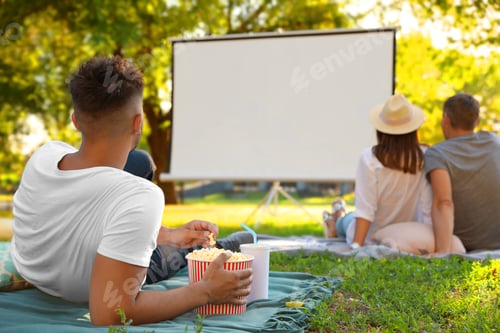 Preview: Young man with popcorn watching movie in open air cinema. Space for text