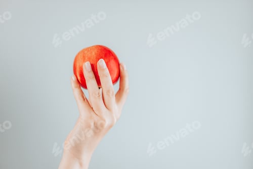 Preview: Red apple in female hand isolated on grey wall background.