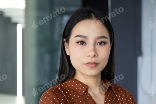 Preview: Confident young Asian businesswoman in modern office setting looking directly at the camera with