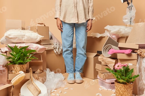 Preview: Cropped shot of unrecognizable woman wears shirt jeans and sneakrs stands indoor around carton boxes