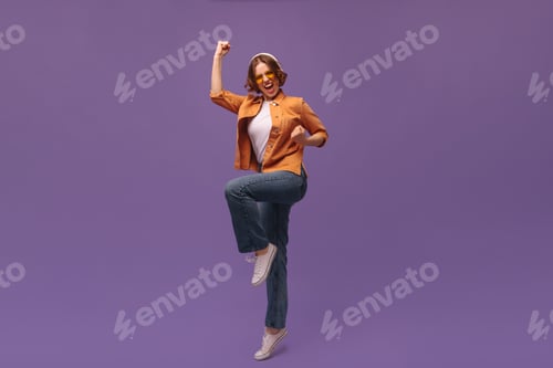 Preview: Full-length portrait of moving young girl at studio. Young short-haired lady wearing orange shirt a