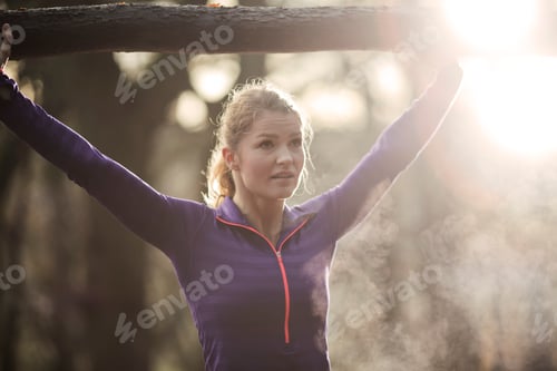 Preview: Young woman in forest arms raised holding tree branch, looking away, condensation from breath
