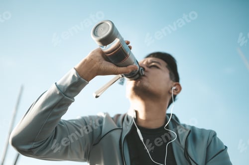 Preview: Young sport man drink water after jogging, running in the park.