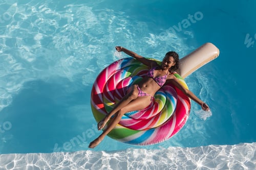Preview: Mixed race woman sunbathing on inflatable in swimming pool