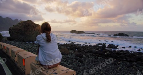 Preview: Young woman tourist on shore enjoing marine views. Rocky seacoast beach. Happy girl looking at Ocean