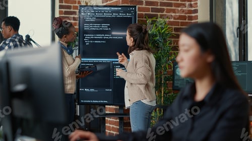 Preview: System engineers comparing source code on wall screen tv analyzing errors using digital tablet